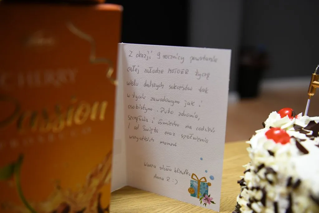 Kartka z życzeniami ustawiona obok urodzinowego tortu MOTOER
